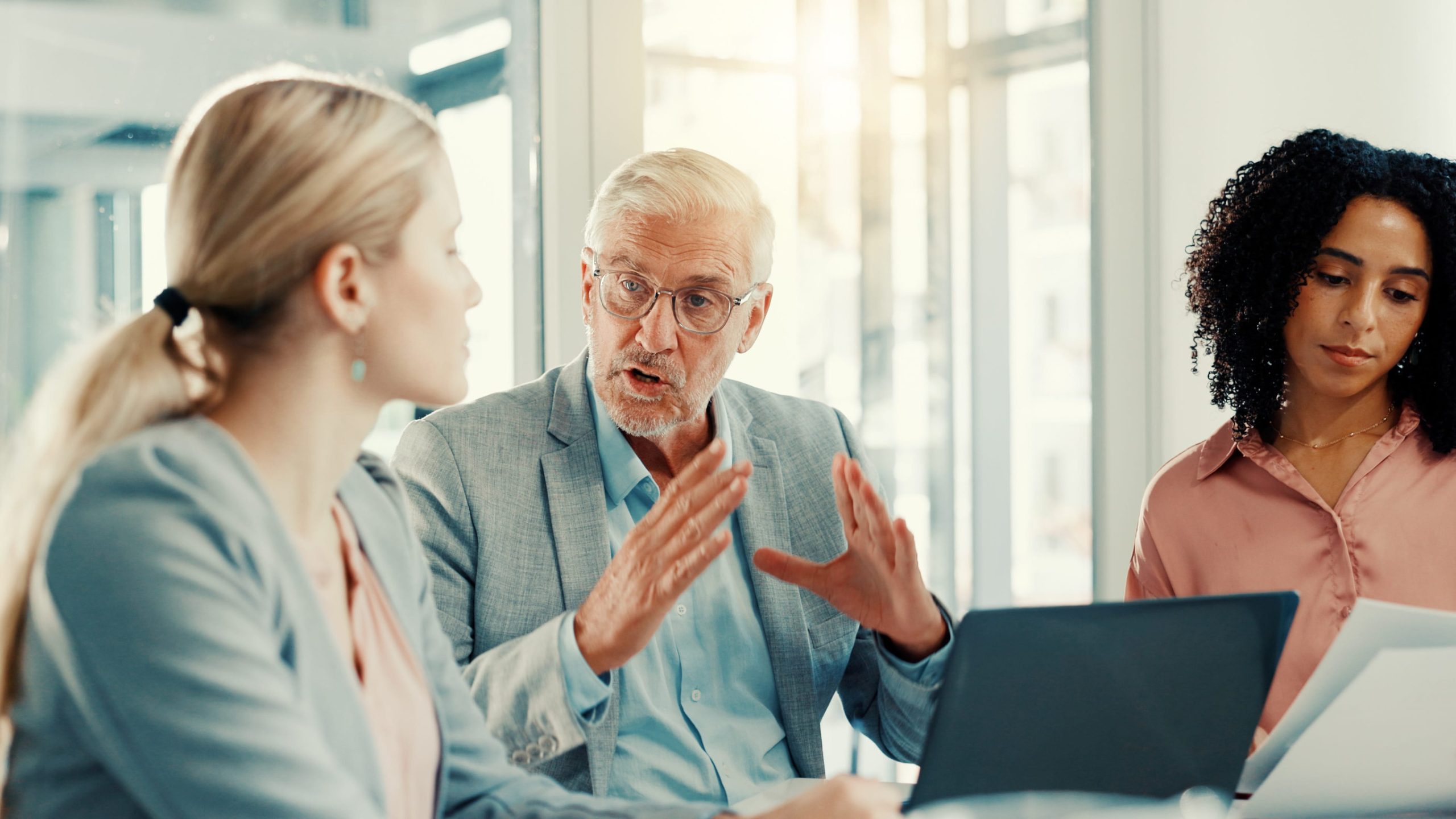 Senior business leader discussing employee benefits and workplace strategy with colleagues during a planning meeting.